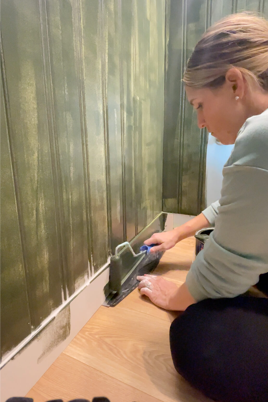 Using a foam roller to paint a beadboard bathroom wall.